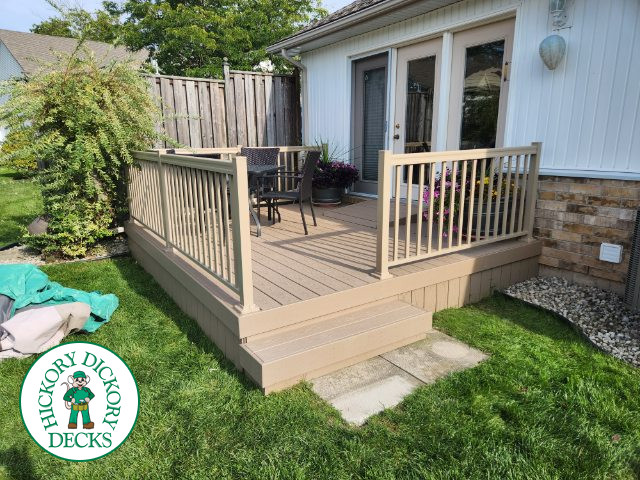 Small beige composite deck with beige railings, accessibility ramp into house.