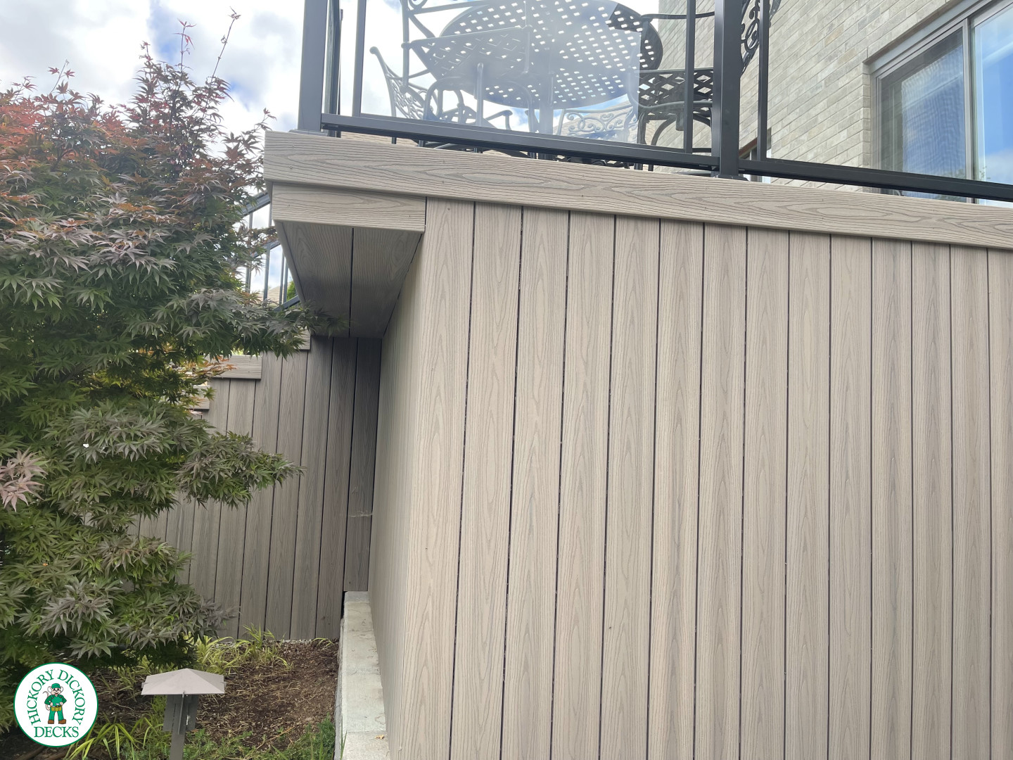 High walk out grey composite deck with aluminum railing on the stairs, and glass style railing around the deck.