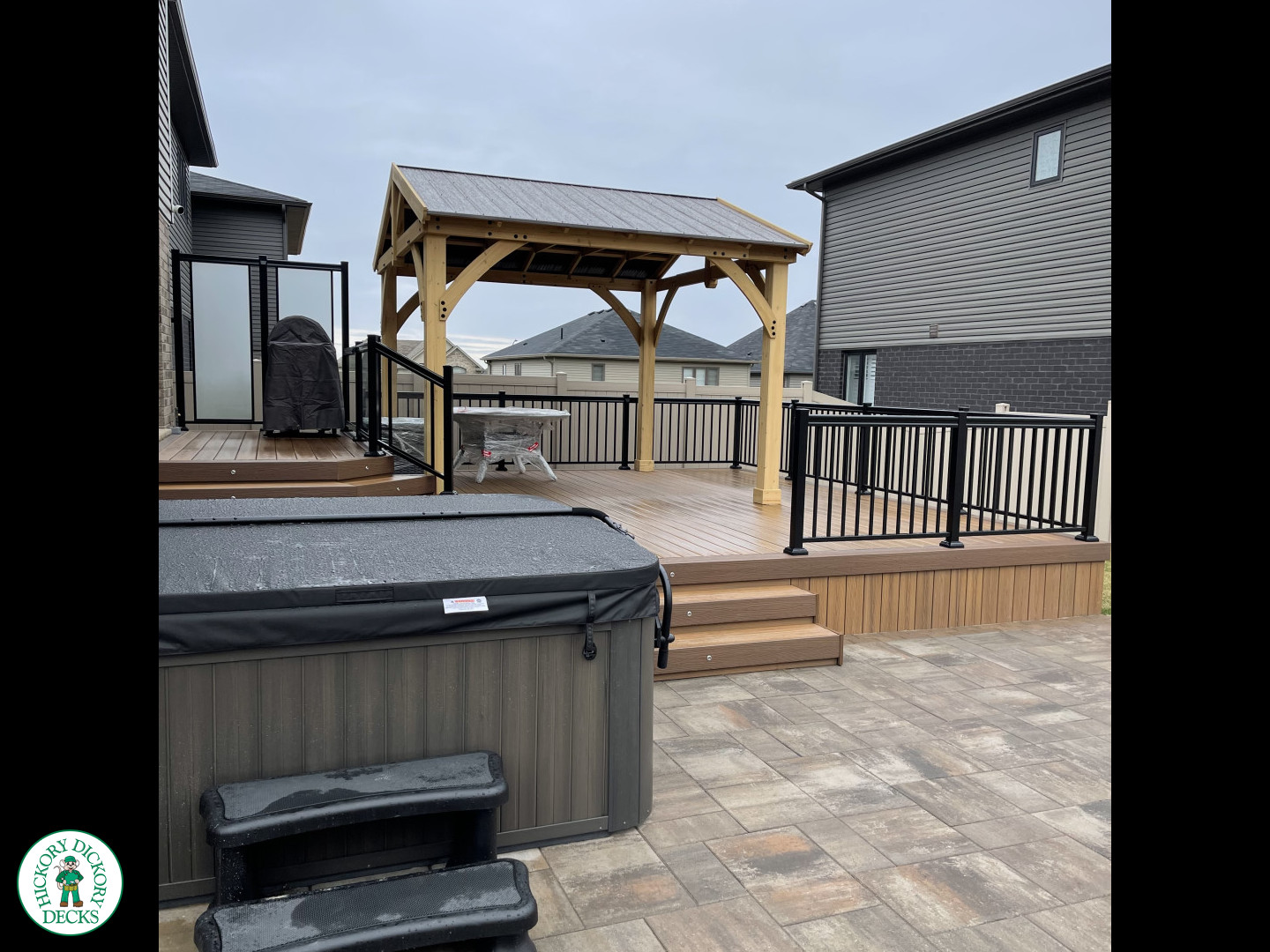 Brown composite deck with a roof structure, glass railings, access to the hot tub, and frosted glass privacy screens.