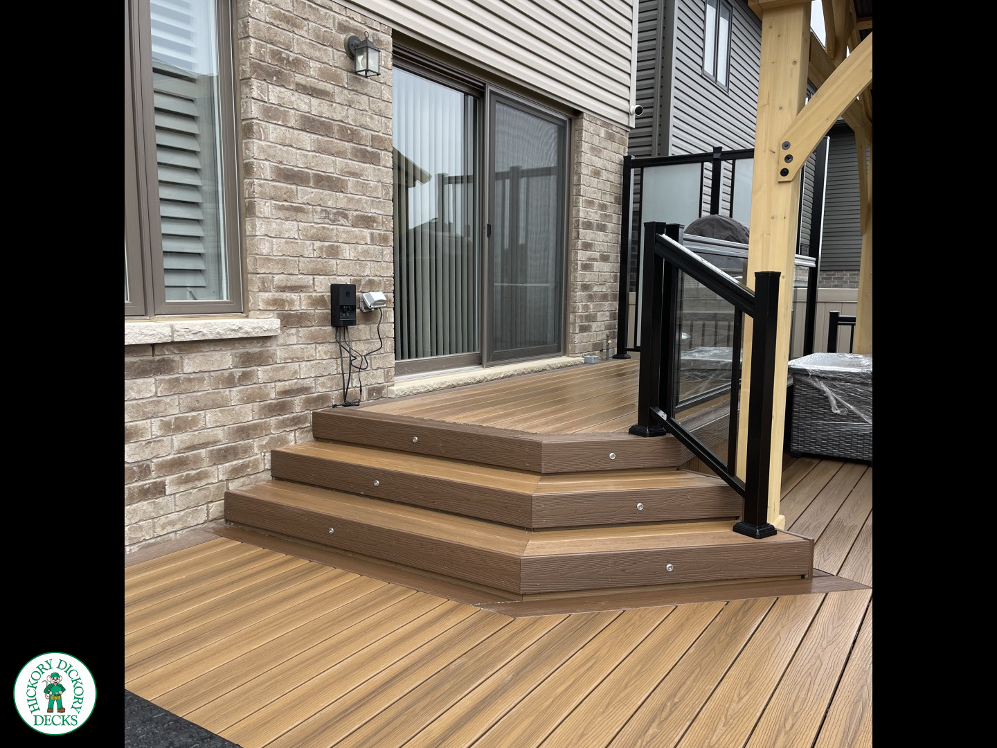 Brown composite deck with a roof structure, glass railings, access to the hot tub, and frosted glass privacy screens.